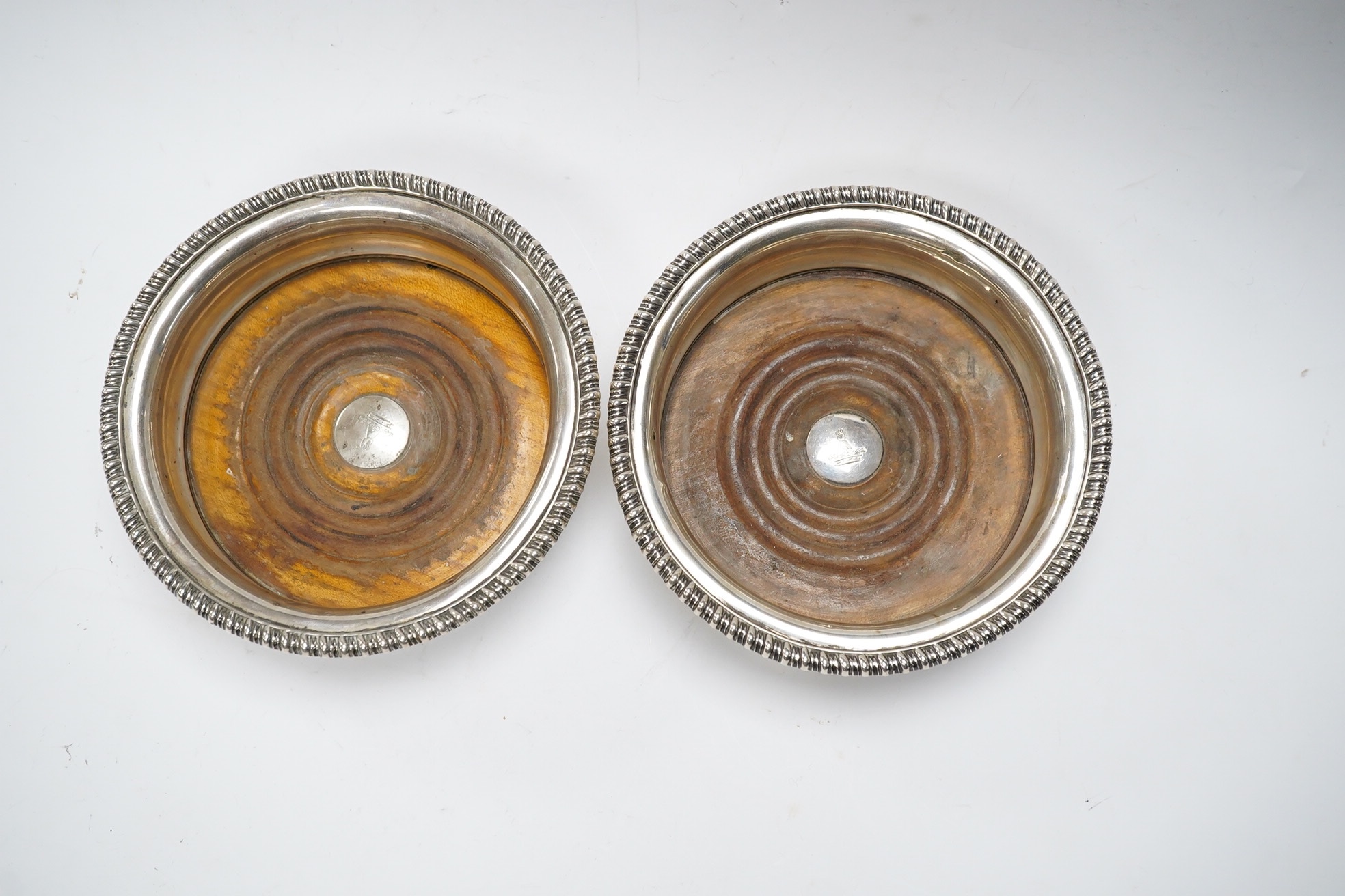 A pair of George III silver wine coasters, by Thomas & John Settle, with gadrooned borders and turned wooden bases, Sheffield, 1821, diameter 15.7cm. Condition - poor to fair